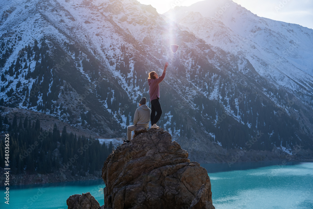 Wall mural Two people hanging on a boulder on a vantage point over mountain lake