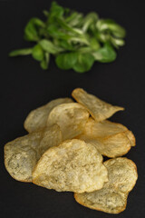 Lettuce leaves and chips on a black background. Healthy and unhealthy food is a contrast. Health care - the right choice of products