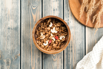 Wooden bowl filled with whole grain granola with berries and nuts. Delicious and healthy breakfast. Tray of spikelets and white towel on rustic wooden surface. Top view - Powered by Adobe