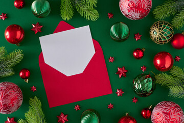 Fototapeta na wymiar Christmas eve concept. Flat lay composition of red and green baubles pine branches star ornaments with paper envelope on deep green background. Creative winter holiday idea.