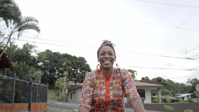 Mujer afro caribe&ntilde;a con una gran sonrisa montada en una bicicleta ofreciendo productos para la venta en la calle con ropa muy colorida