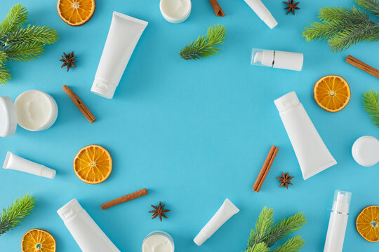 Natural cosmetics concept. Top view photo of cosmetic bottles without label, christmas tree branches and dried orange slices cinnamon sticks on pastel blue background with border arrangement.