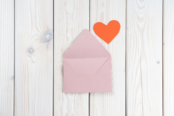 Pink opened envelope on white wooden background. Red cardboard heart is taken out of Valentine envelope. Copy space. Love, valentine, confession of feelings. Top view