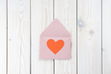 Pink opened envelope on white wooden background. Red cardboard heart is taken out of Valentine envelope. Copy space. Love, valentine, confession of feelings. Top view