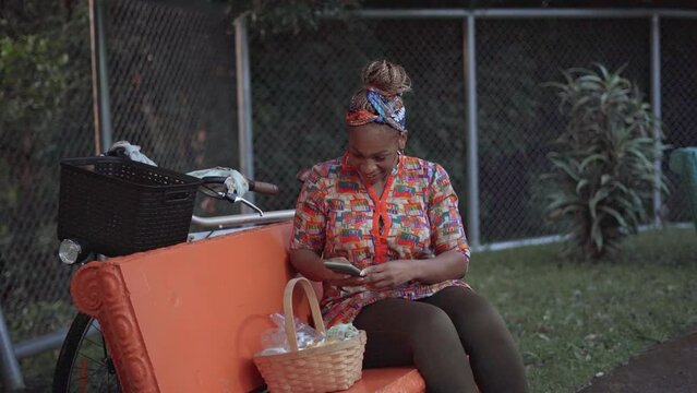 Imagen de una mujer afro caribe&ntilde;a sentada en el exterior tom&aacute;ndole fotos a una canasta con productos para la venta  en su comunidad