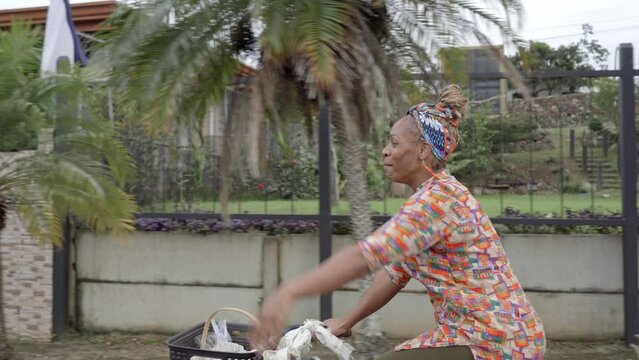 video de una hermosa mujer morena con cabello afro y una pa&ntilde;oleta en su cabeza, muy sonriente vendiendo sus productos mientras se transporta en una bicicleta