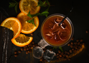 Coffee cocktail with ice decorated with sliced orange and mint, black background