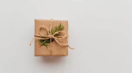 Kraft cardboard gift box tied with rough jute rope on gray wooden background with branches of Christmas tree and Christmas decorations