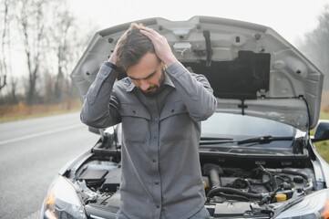 Sad driver holding his head having engine problem standing near broken car on the road. Car breakdown concept