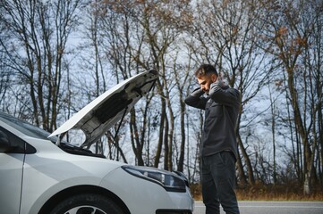 Sad driver holding his head having engine problem standing near broken car on the road. Car breakdown concept