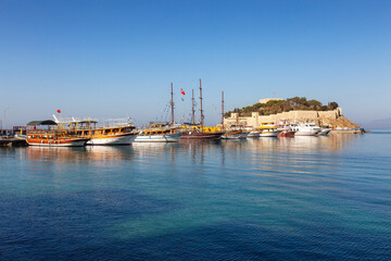 Fototapeta premium Boats at Marina with Castle on the Coast in a Touristic Town by the Aegean Sea. Kusadasi, Turkey. Sunny Morning Sunrise.