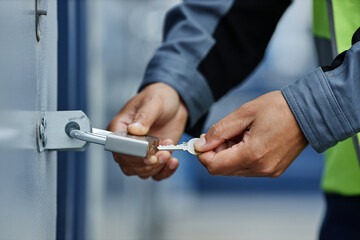 Close up of worker opening hanging lock with key on container door in shipping docks, copy space