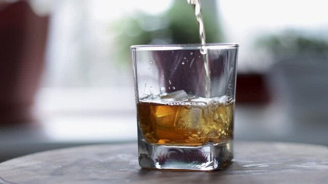Two ice cubes fall into a glass of bourbon.
