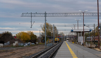 Nowo remontowany tor i peron kolejowy w pobliżu stacji kolejowej  . W tle zachmurzone błękitne niebo .