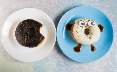 Chocolate and white glazed donuts lay on plates. Top view on funny doughnut with eyes, legs, hands. Creative food photo, flatly