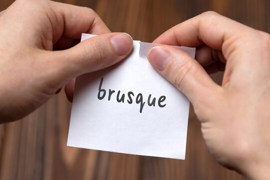 Hands of a man tearing a piece of paper with inscription brusque