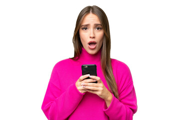 Young beautiful caucasian woman over isolated background looking at the camera while using the mobile with surprised expression