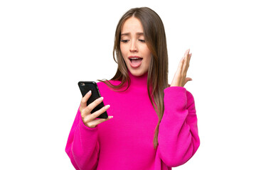 Naklejka premium Young beautiful caucasian woman over isolated background looking at the camera while using the mobile with surprised expression