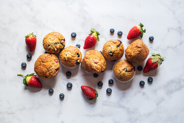 Blueberry and strawberry muffins on a white marble background. - 548052732