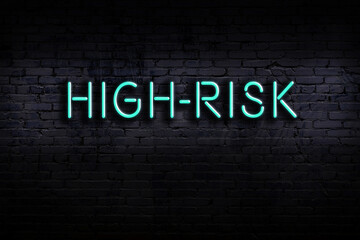 Neon sign. Word high-risk against brick wall. Night view