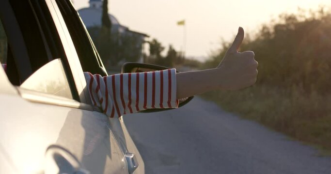 Driver hand shows thumbs up from right side car window, reveal panning shot.