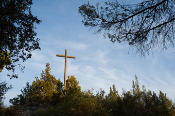 Crucifijo católico de grandes dimensiones en el bosque recibiendo luz del sol al atardecer