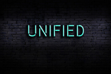 Neon sign. Word unified against brick wall. Night view
