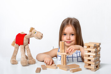 Studio shot of a  little smiling girl with long blonde hair  sitting on the white table and plaing...