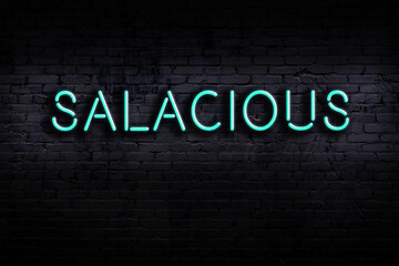 Night view of neon sign on brick wall with inscription salacious - obrazy, fototapety, plakaty