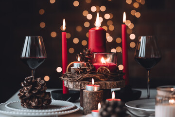 Rustic table decor for Christmas or New Year family dinner. Centrepiece with red candle, dry orange, cone, cinnamon, anise. Zero waste eco-friendly home. Cozy atmosphere, dark background. Close up