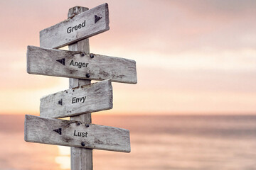 greed anger envy lust text written on wooden signpost outdoors at the beach during sunset - obrazy, fototapety, plakaty