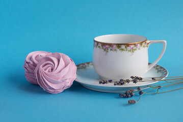 Homemade pink zephyr or marshmallow with white porcelain cup and lavander close to. Isolated on blue background. Sweet Meringue dessert. Valentineâ€™s or Mothers Day concept.