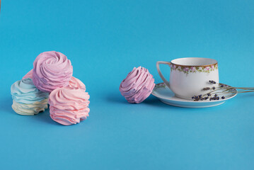 Homemade pink zephyr or marshmallow with white porcelain cup and lavander close to. Isolated on blue background. Sweet Meringue dessert. Valentine’s or Mothers Day concept.