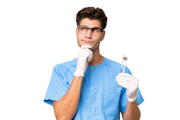 Young dentist man holding tools over isolated background having doubts and thinking