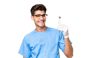 Young dentist man holding tools over isolated background looking to the side and smiling