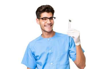 Young dentist man holding tools over isolated background looking to the side and smiling