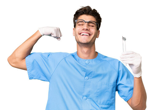 Young dentist man holding tools over isolated background doing strong gesture