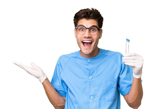 Young dentist man holding tools over isolated background with shocked facial expression