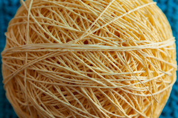 Close-up of yellow color yarn clew. Blurry background of crochet of pattern of jeans color.