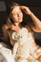 Portrait girl is waking up in morning stretches in bed and sun shines from the window. Happy young woman greets new sunny day