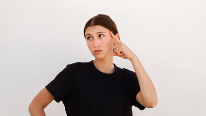 Portrait of thoughtful young woman thinking or planning. Caucasian woman wearing black T-shirt looking away and pointing at her head. Idea and solution concept