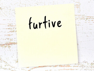 Yellow sticky note on wooden wall with handwritten word furtive