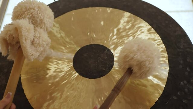Gong and gong mallets, close up. Female hands hit the gong with soft hammers