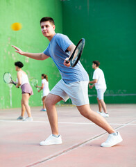 Sporty young man playing popular team game frontenis at open-air fronton court on summer day, ready...