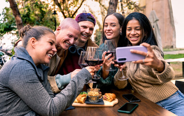 Friends taking selfie - drinking red wine and eating snacks - People having fun at patio - Lifestyle concept with happy men and women at cafe bar - Focus on glasses