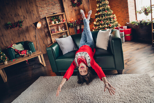 Full body length photo of funky excited woman wear ugly christmas sweater lying down childish new year holidays vacation indoors near fir tree garland