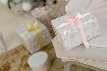 Beautiful Christmas present with silver snowlakes and pink ribbon lying on a chair near christmas tree