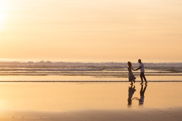 Fond couple walking on beach at sunset. Man and woman in casual clothes running along water at...