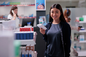 Asian cheerful client holding medicinal supplements, buying pills for immune system. Pharmacy client shopping for medicine, drugs, vitamines, in drugstore. Health care support service