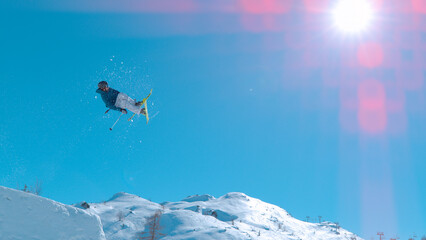 LOW ANGLE VIEW Male skier jumping big air kicker at snow park in snowy ski area - obrazy, fototapety, plakaty